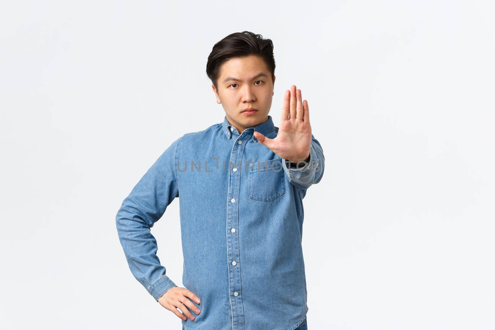 Serious strict asian man extending hand to shop stop gesture, scolding person or disagree, prohibit action, forbid doing something bad, standing over white background and give warning.