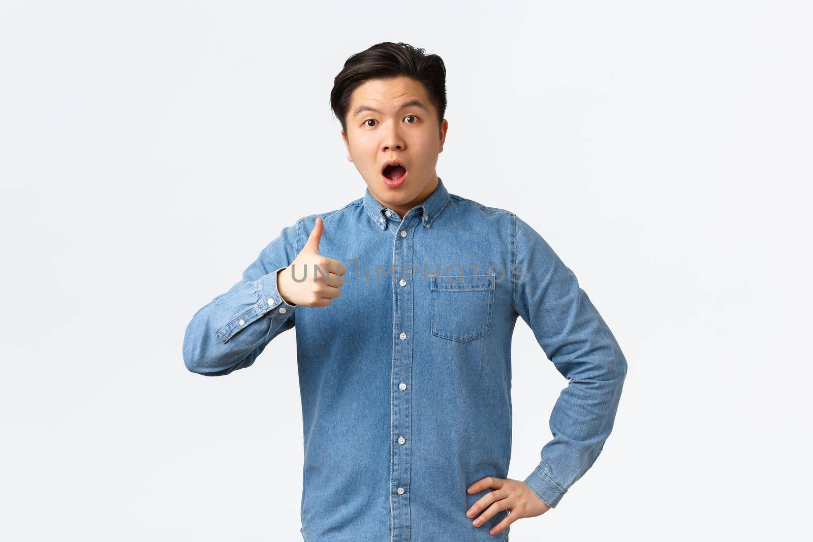 Surprised and impressed asian male student open mouth fascinated, showing thumbs-up astounded, saying wow, rate great work, saying well done or good job, standing white background.
