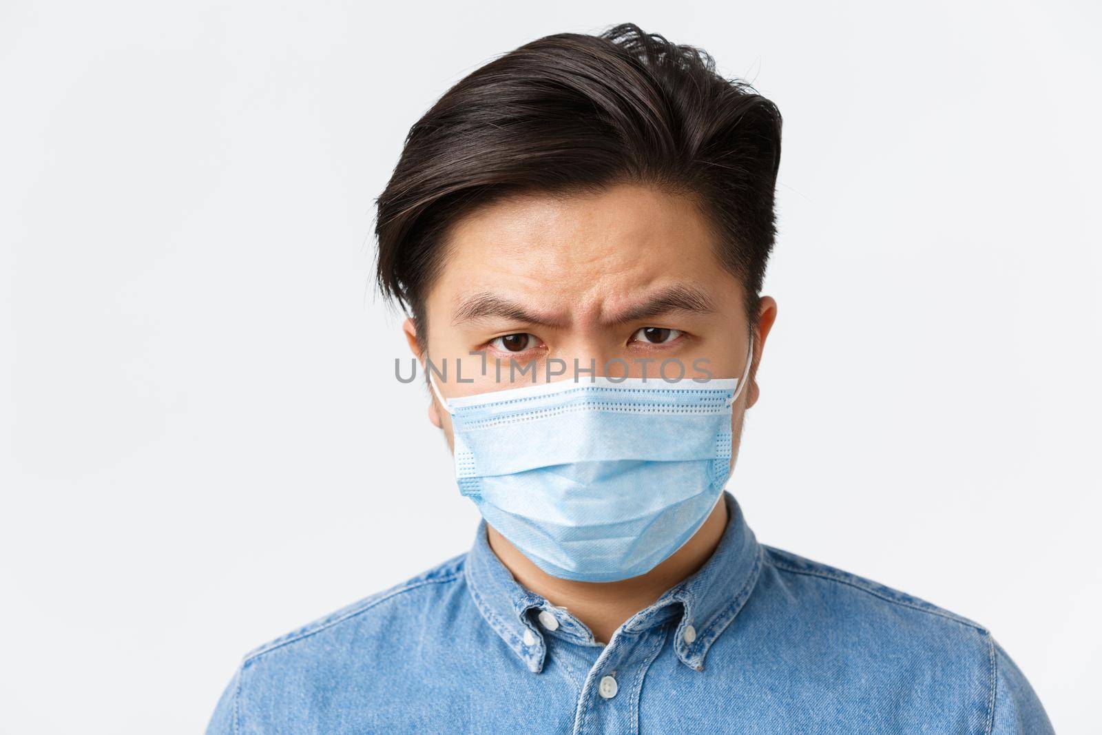 Coronavirus, social distancing and lifestyle concept. Close-up of angry and upset asian man in medical mask frowning disappointed, looking at person not using protective measures during covid-19 by Benzoix