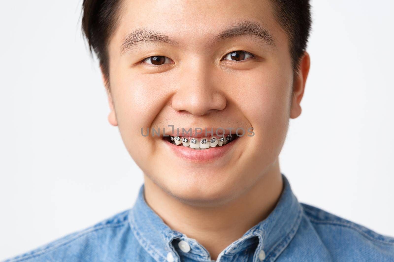 Orthodontics and stomatology concept. Headshot of happy asian man smiling, showing dental braces, recommend clinic, satisfied with good results, standing white background pleased by Benzoix