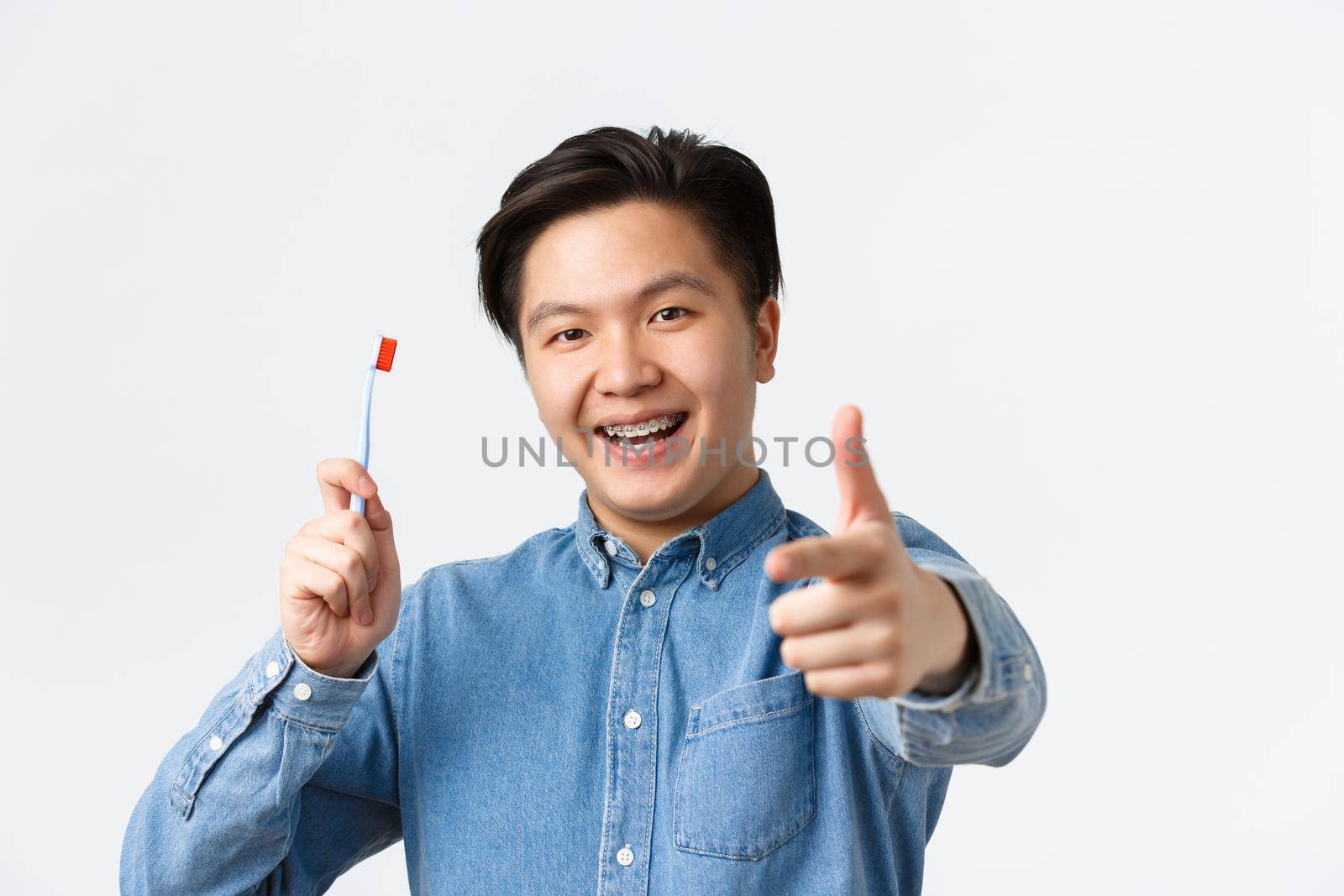 Orthodontics, dental care and hygiene concept. Close-up of happy and pleased asian man recommend stomatology clinic, showing toothbrush and thumbs-up explain how take care of teeth braces by Benzoix