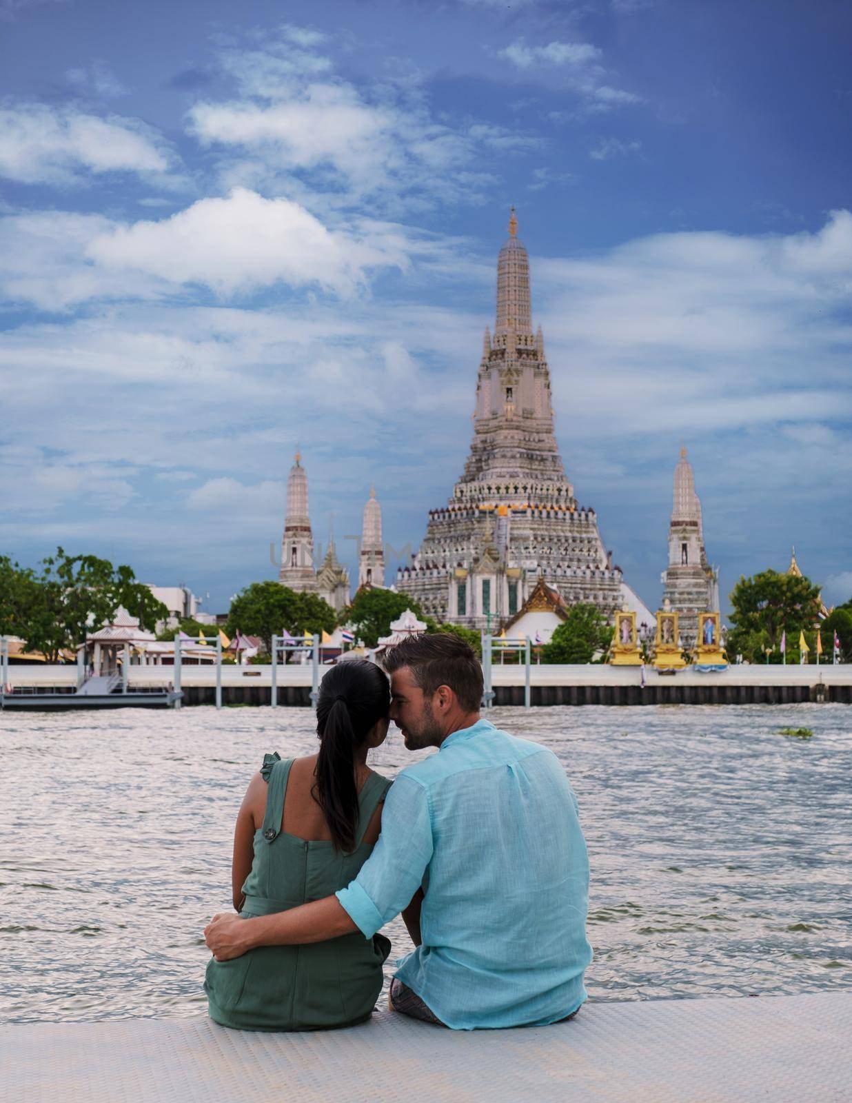 Wat Arun temple Bangkok Thailand, Temple of Dawn, Buddhist temple alongside Chao Phraya River.Beautiful Wat Arun at dusk evening sunset, couple Asian woman and European men watching sunset