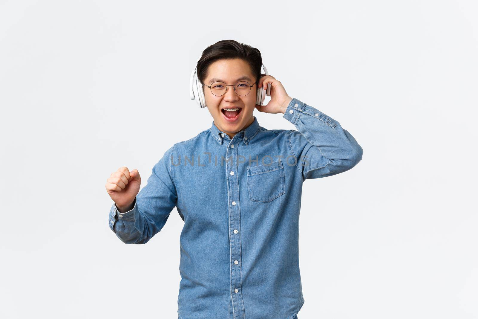 Lifestyle, leisure and technology concept. Joyful happy asian man in glasses, dancing carefree to awesome sound of music, great earphones quality, wearing wireless headphone, enjoying listening song by Benzoix