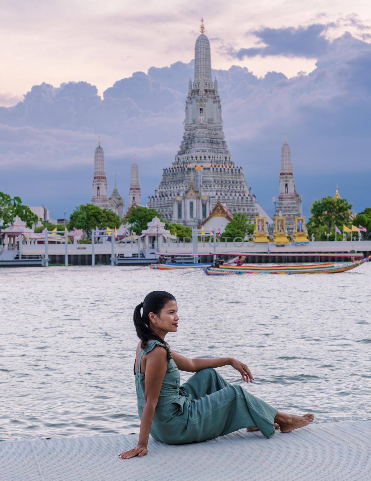 Wat Arun temple Bangkok Thailand, Temple of Dawn, Buddhist temple alongside Chao Phraya River.Beautiful Wat Arun at dusk evening sunset, Asian woman watching sunset alongside Chao Phraya River