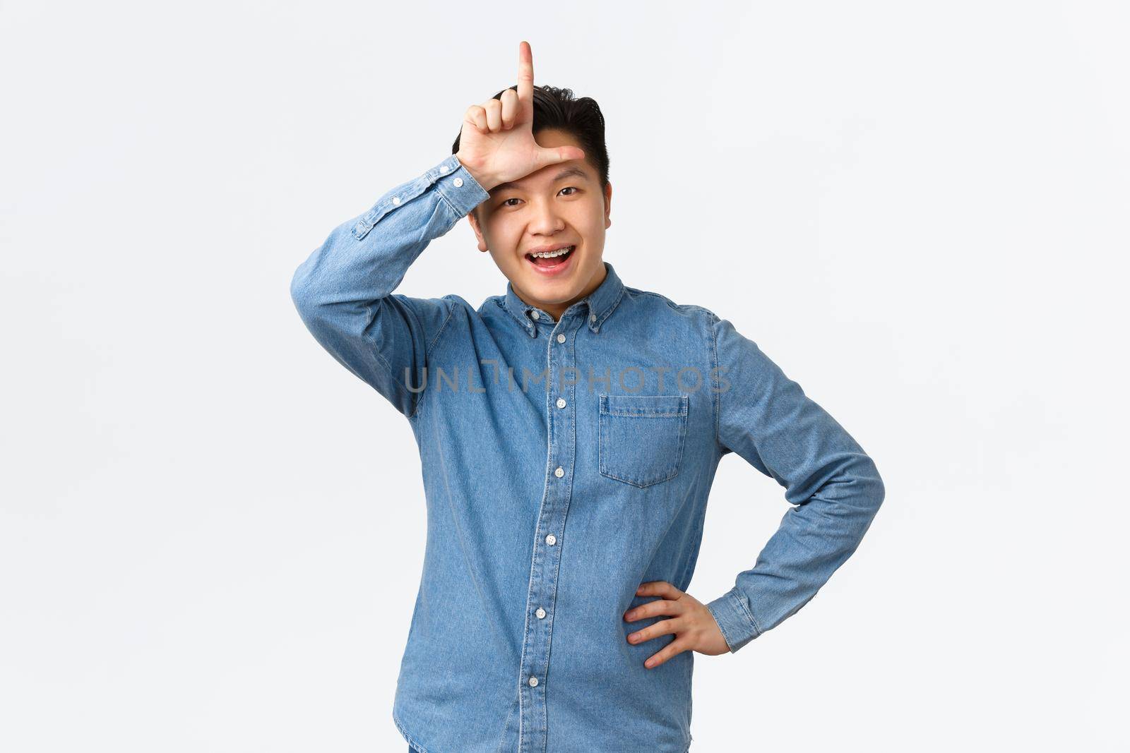 Happy rejoicing asian guy mocking lost team, showing loser gesture and smiling, making fun of rival, standing satisfied and proud of winning over white background, laughing arrogant.