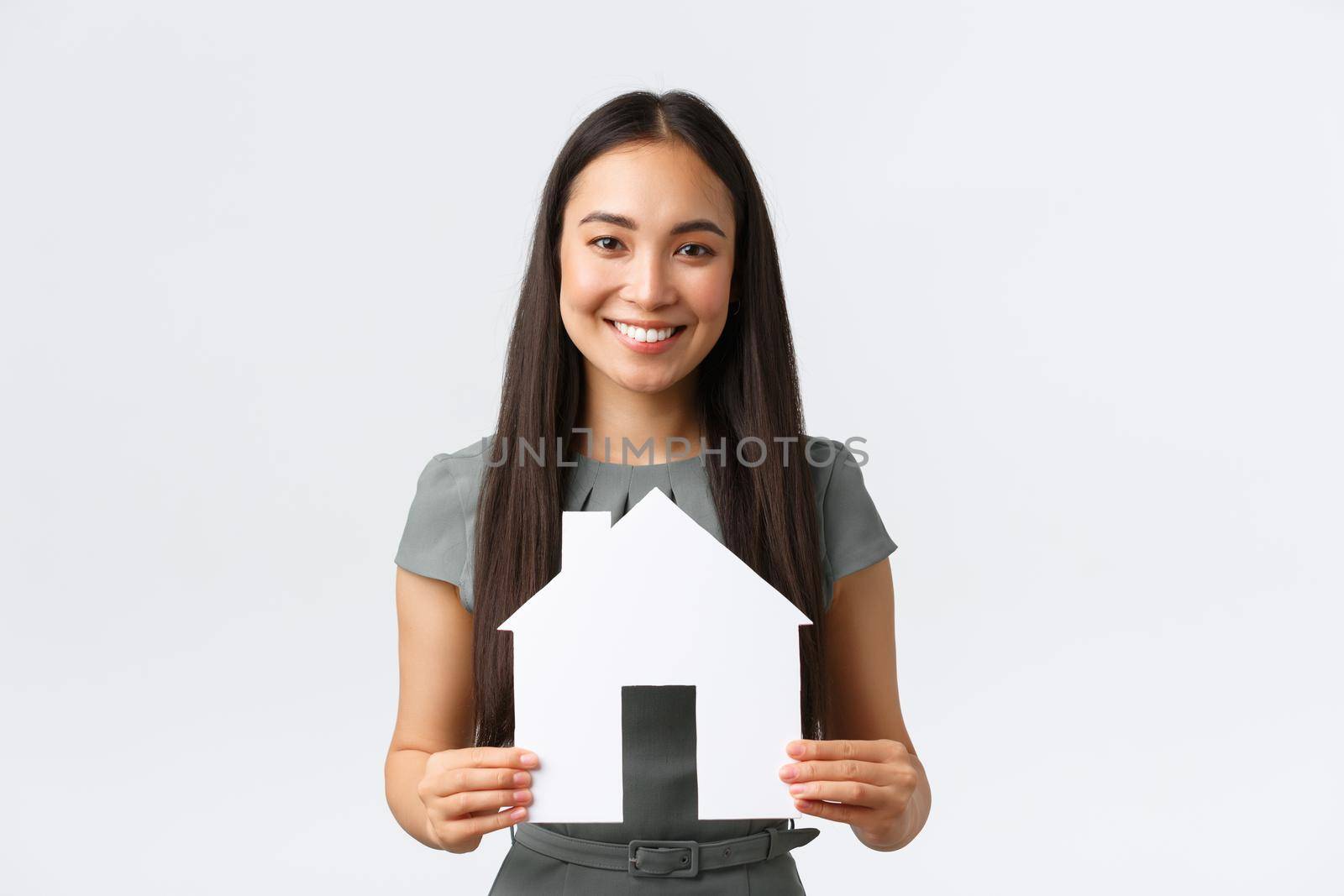 Insurance, loan, real estate and family concept. Smiling asian woman buying home, holding paper house in hands and smiling, paying debt, standing white background happy.