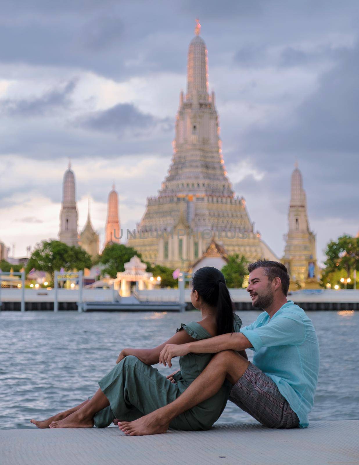 Wat Arun temple Bangkok Thailand, Temple of Dawn, Buddhist temple alongside Chao Phraya River.Beautiful Wat Arun at dusk evening sunset, couple Asian woman and European men watching sunset