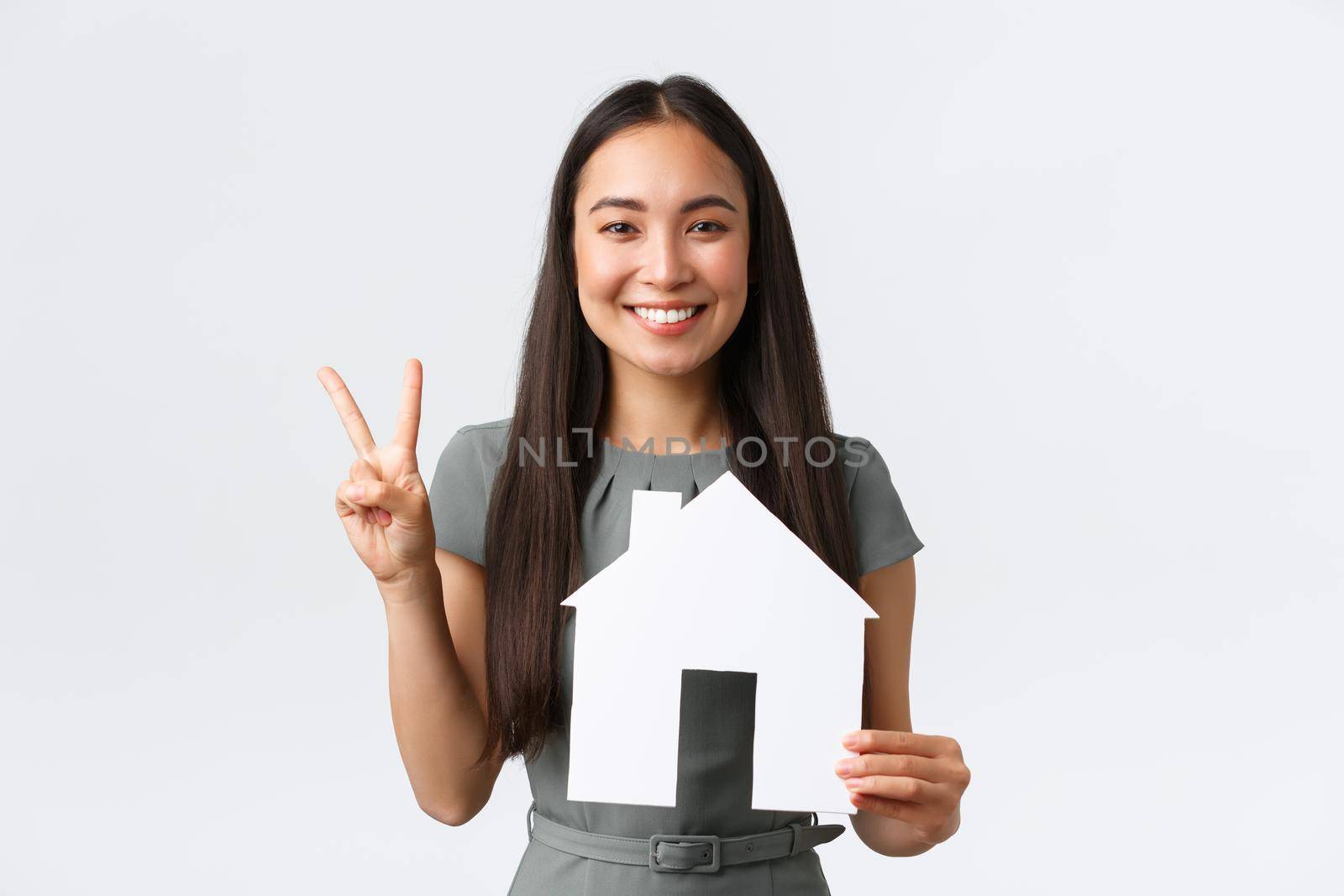 Insurance, loan, real estate and family concept. Smiling attractive asian woman selling or buying apartment, showing peace kawaii sign and paper house, saleswoman showing home, white background by Benzoix