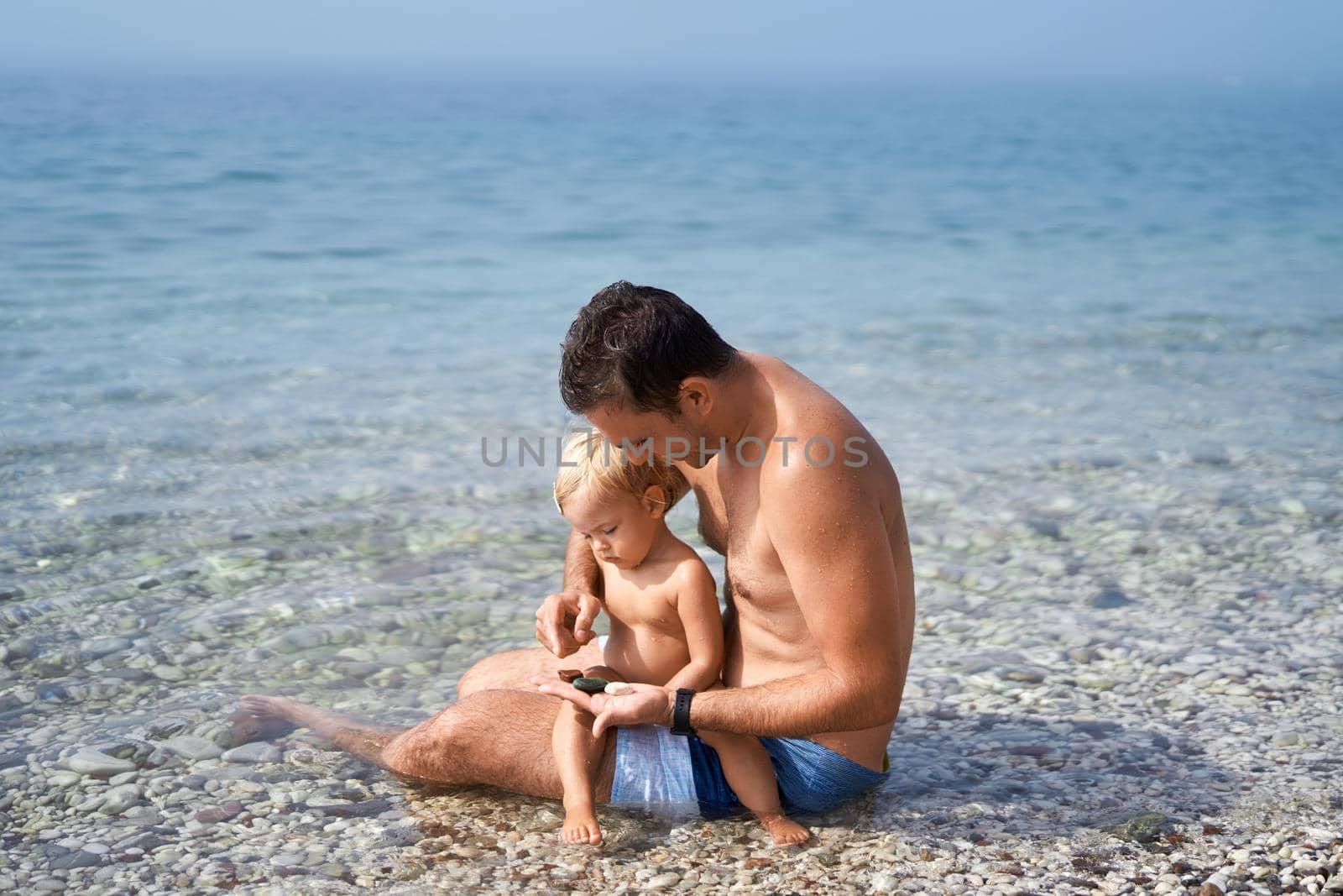 Dad and a little girl are sitting and sorting out sea pebbles. High quality photo