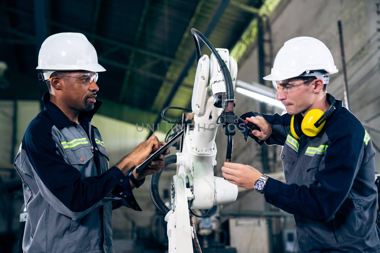 Factory workers working with adept robotic arm in a workshop by biancoblue