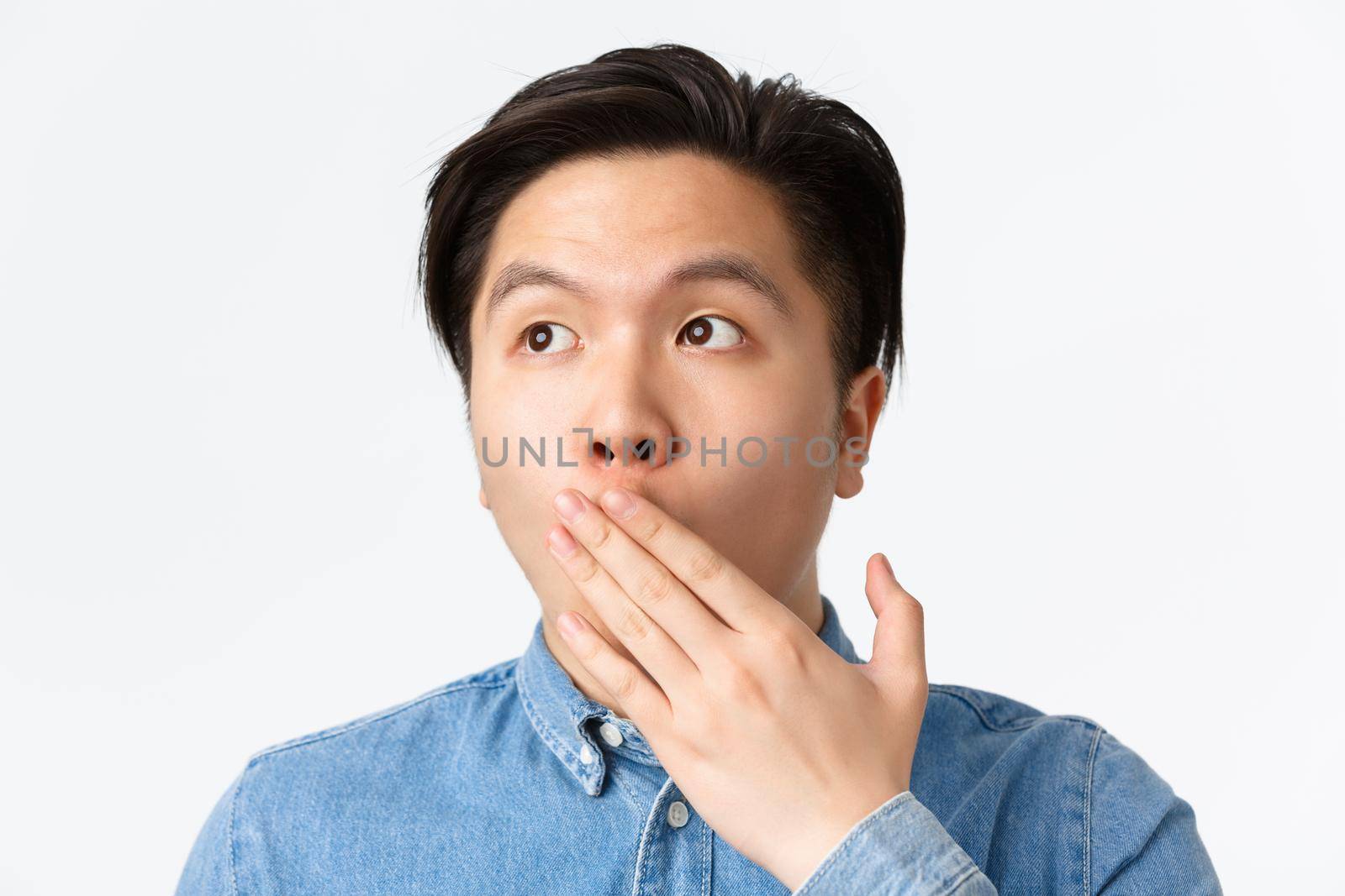 Close-up of shocked and startled young asian guy gasping of amazement, looking upper left corner, cover opened mouth in awe, standing impressed over white background by Benzoix