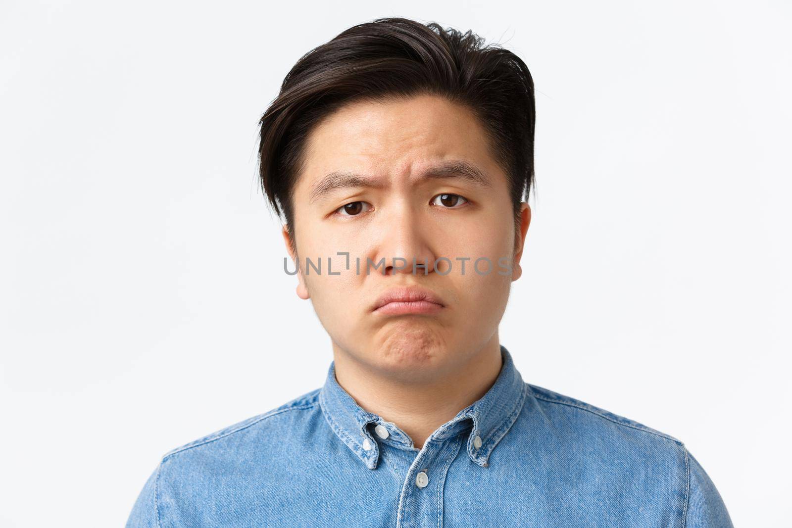 Orthodontics, dental care and stomatology concept. Close-up of gloomy and sad cute asian guy sulking, looking upset at camera, feeling lonely or distressed, standing white background in bad mood.