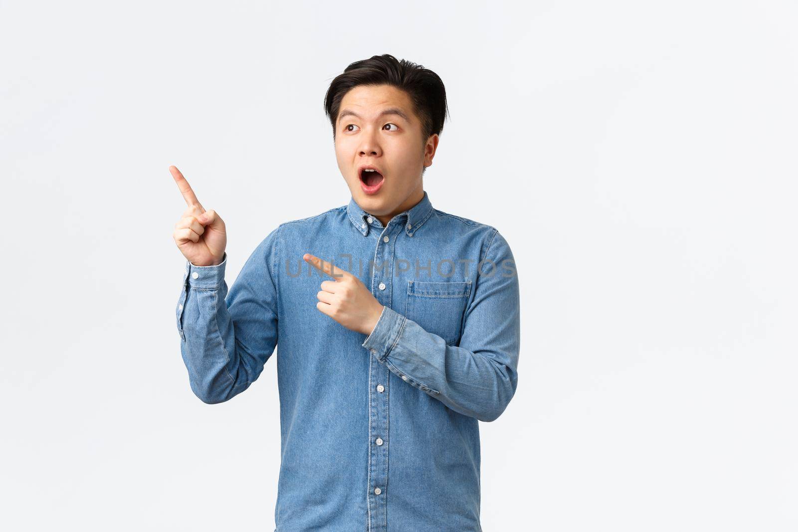 Impressed and astounded young asian man react to fantastic news, open mouth fascinated, pointing and looking upper left corner amazing advertisement banner, standing white background.