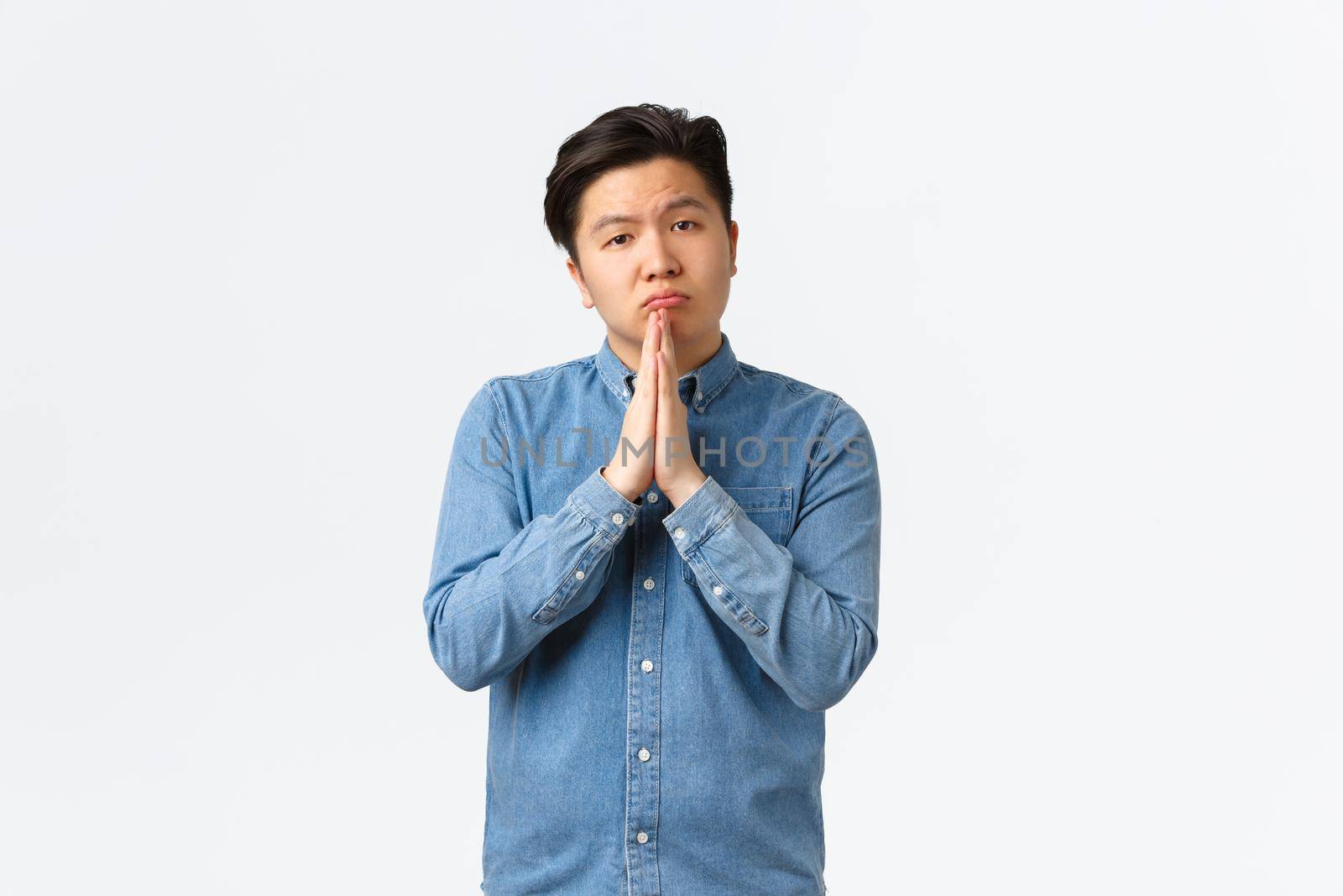 Sad gloomy asian male asking for help, begging favour, standing over white background and hold hands together in plead, supplicating, lending money from friend, apoligizing.