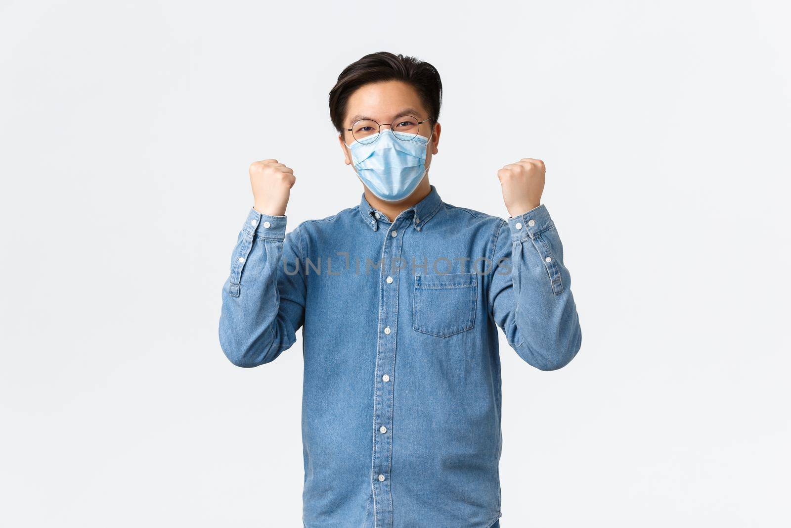 Covid-19, preventing virus, and social distancing at workplace concept. Successful winning asian man encourage team wear medical masks to fight coronavirus, raising hands up triumphing.