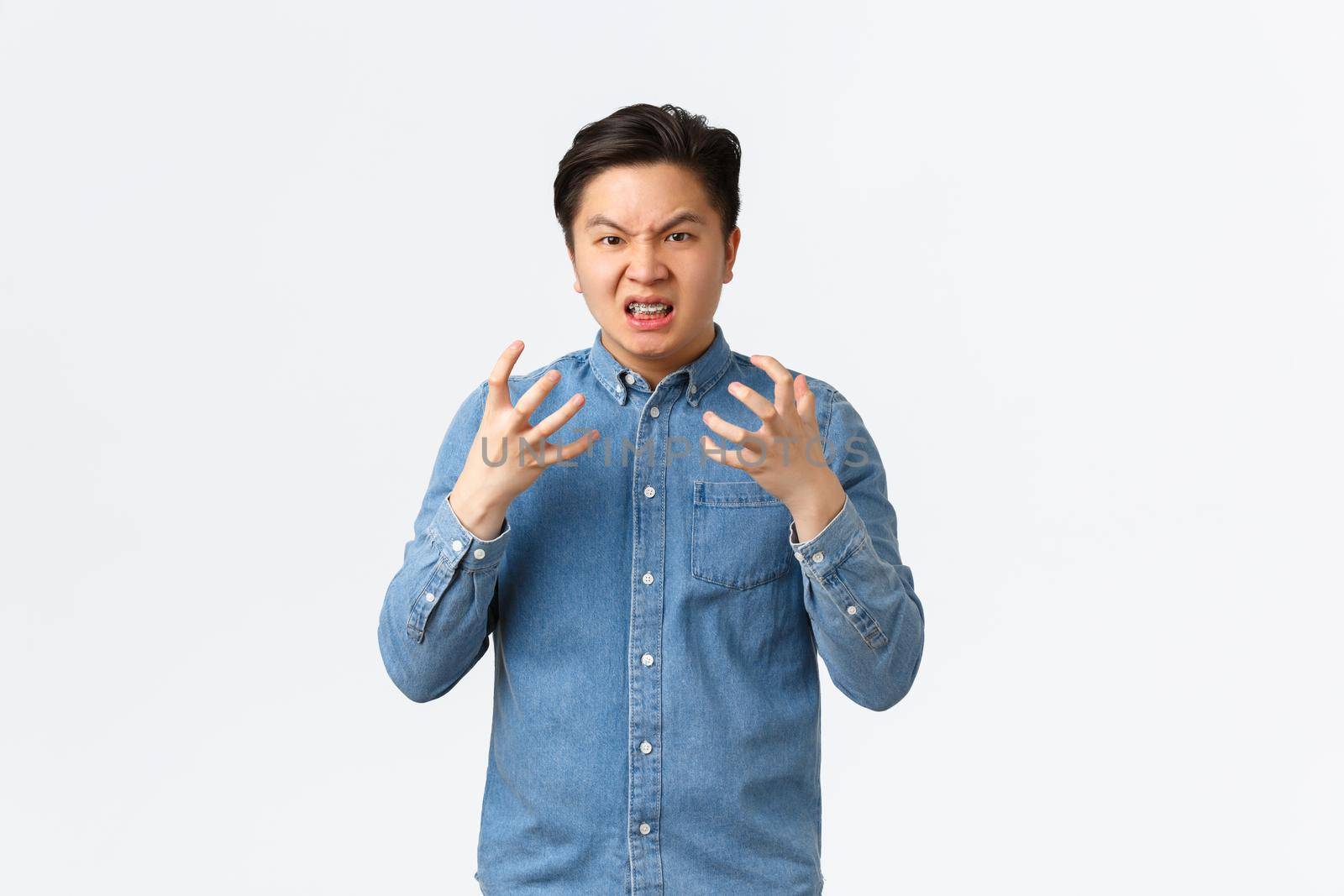 Outraged aggressive and pissed-off asian man shaking hands frustrated and mad, frowning and grimacing, swearing angry at someone, feeling furious, standing white background.