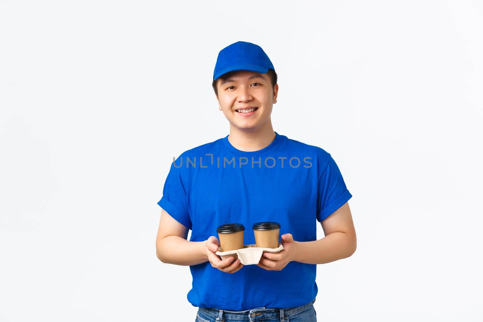 Online orders, takeaway and employees concept. Friendly smiling asian delivery man, salesman in blue uniform carry cups with coffee, handing drinks to clients, standing white background.