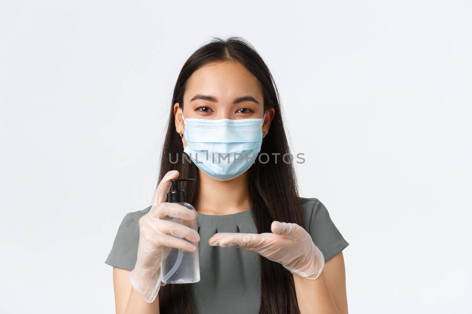Small business owners, covid-19, preventing virus measures concept. Close-up of smiling asian woman in medical mask and gloves desinfecting it with hand sanitizer before packing customer order.