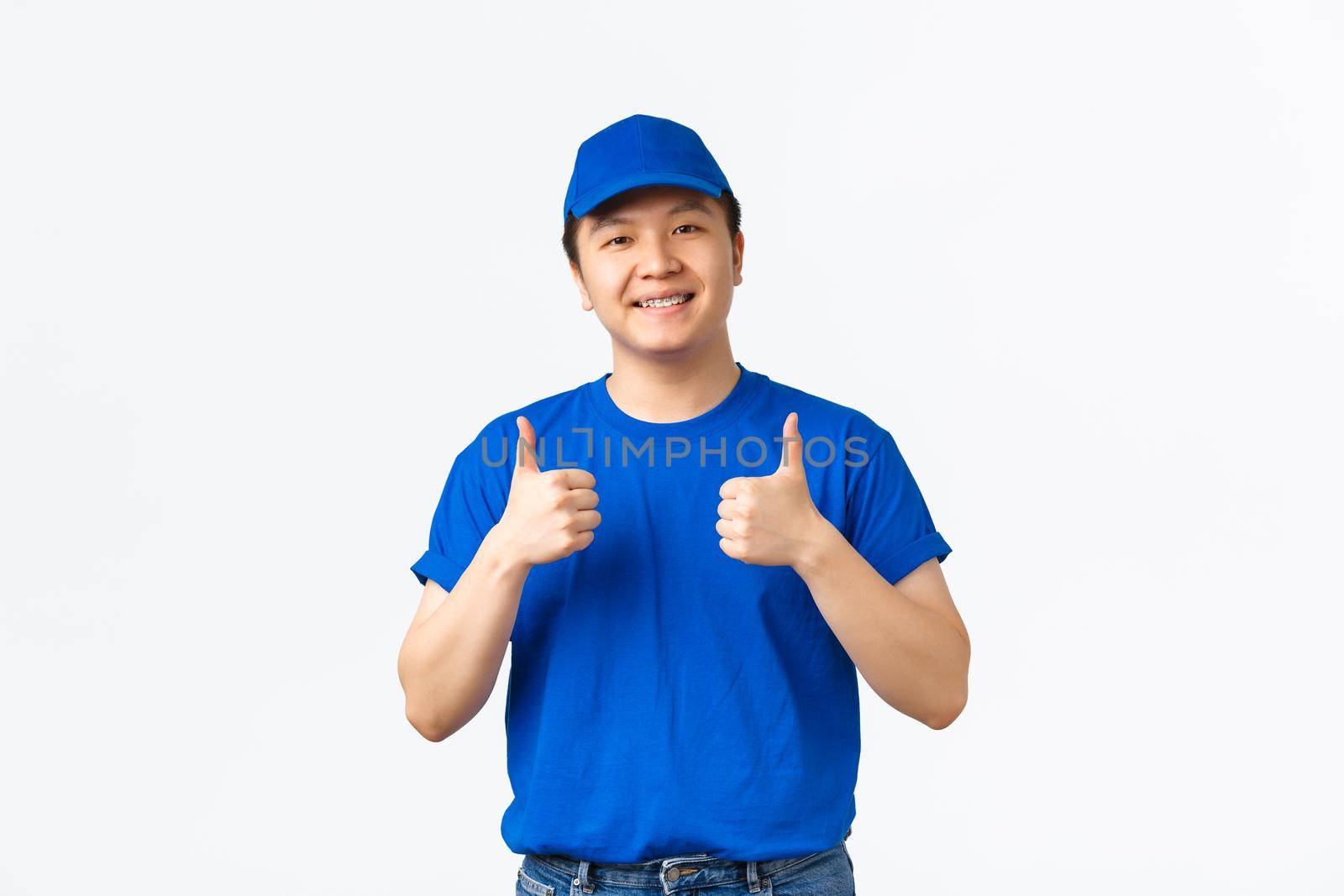 Friendly cheerful asian courier in blue uniform, smiling with braces, showing thumbs-up, guarantee, provide best offers, fast delivery and cheap prices, recommend shipping company.