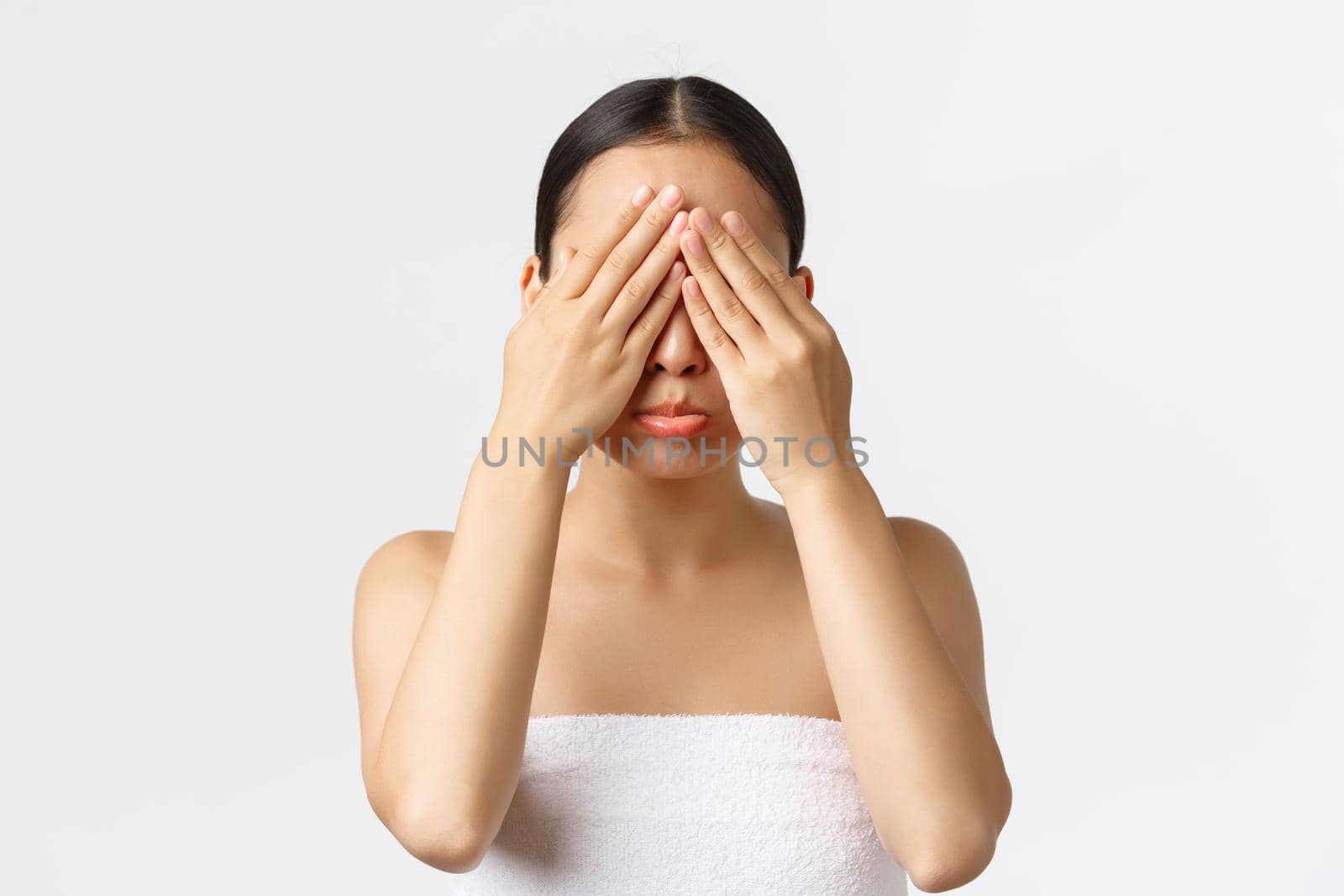 Beauty, cosmetology and spa salon concept. Sad pouting asian girl refuse open eyes, sulking depressed, standing in bath towel, have bad experience with skincare product, white background by Benzoix
