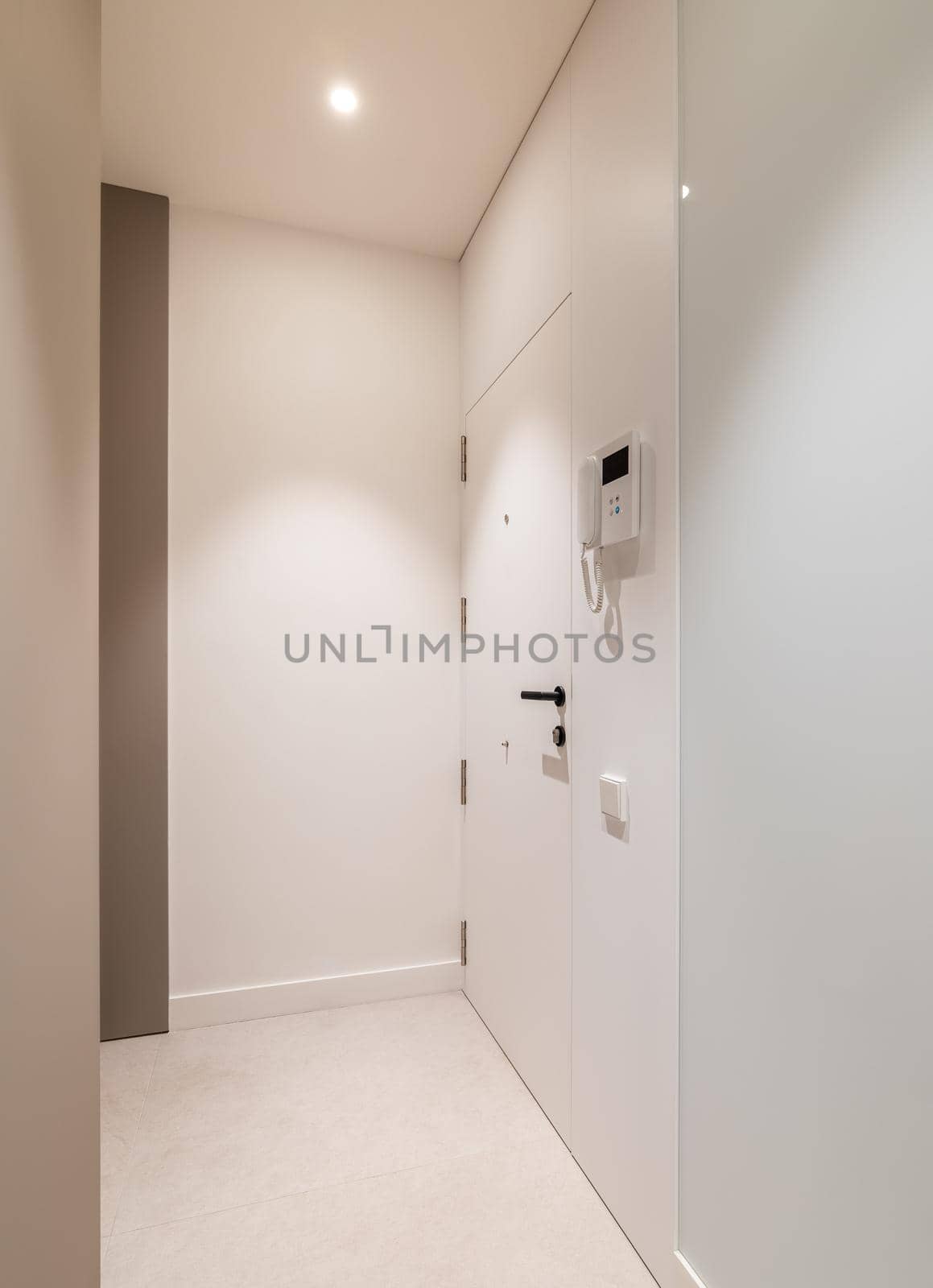 Vertical view of entrance hall area in modern refurbished apartment. White walls and door with intercom system
