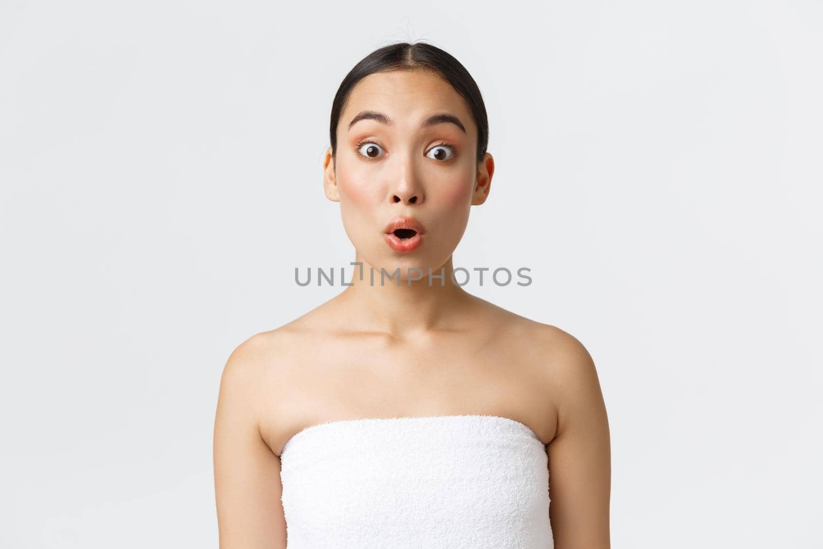 Impressed and curious asian girl hear interesting promo offer, standing in towel over white background, advertisement of spa salon, beauty products, skincare supplies, white background.