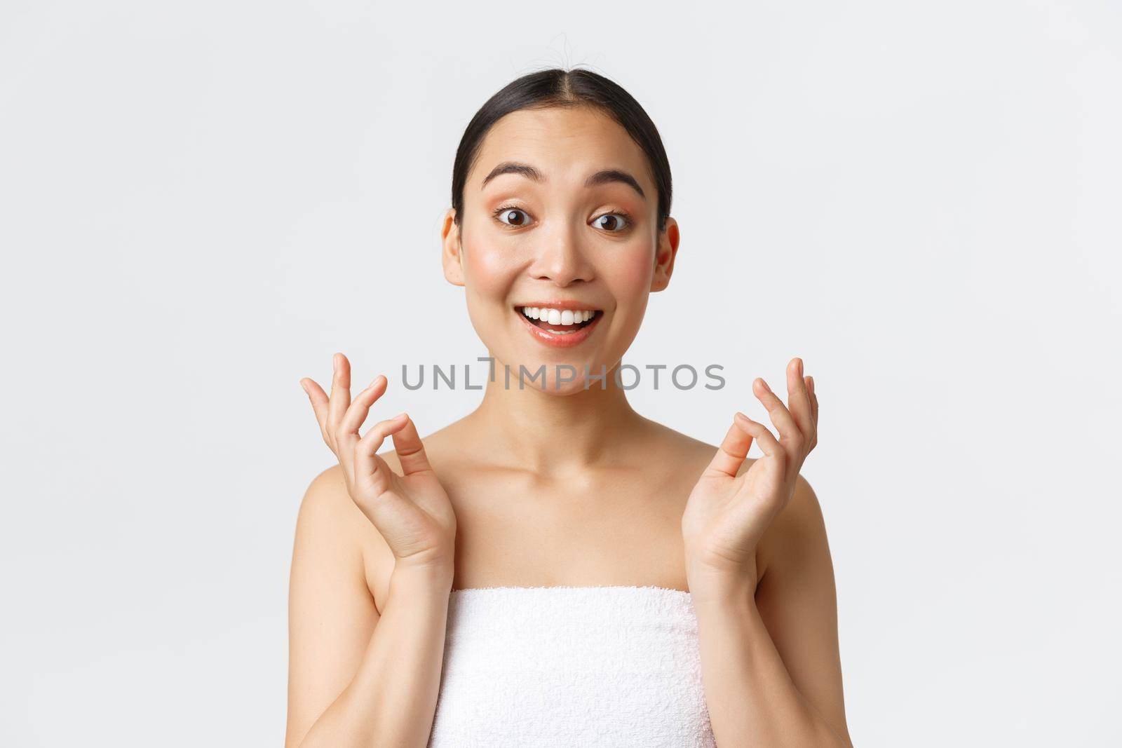 Beauty, cosmetology and spa salon concept. Surprised and happy beautiful asian girl in towel react to clean perfect skin after skincare or massage therapy, look impressed and satisfied.