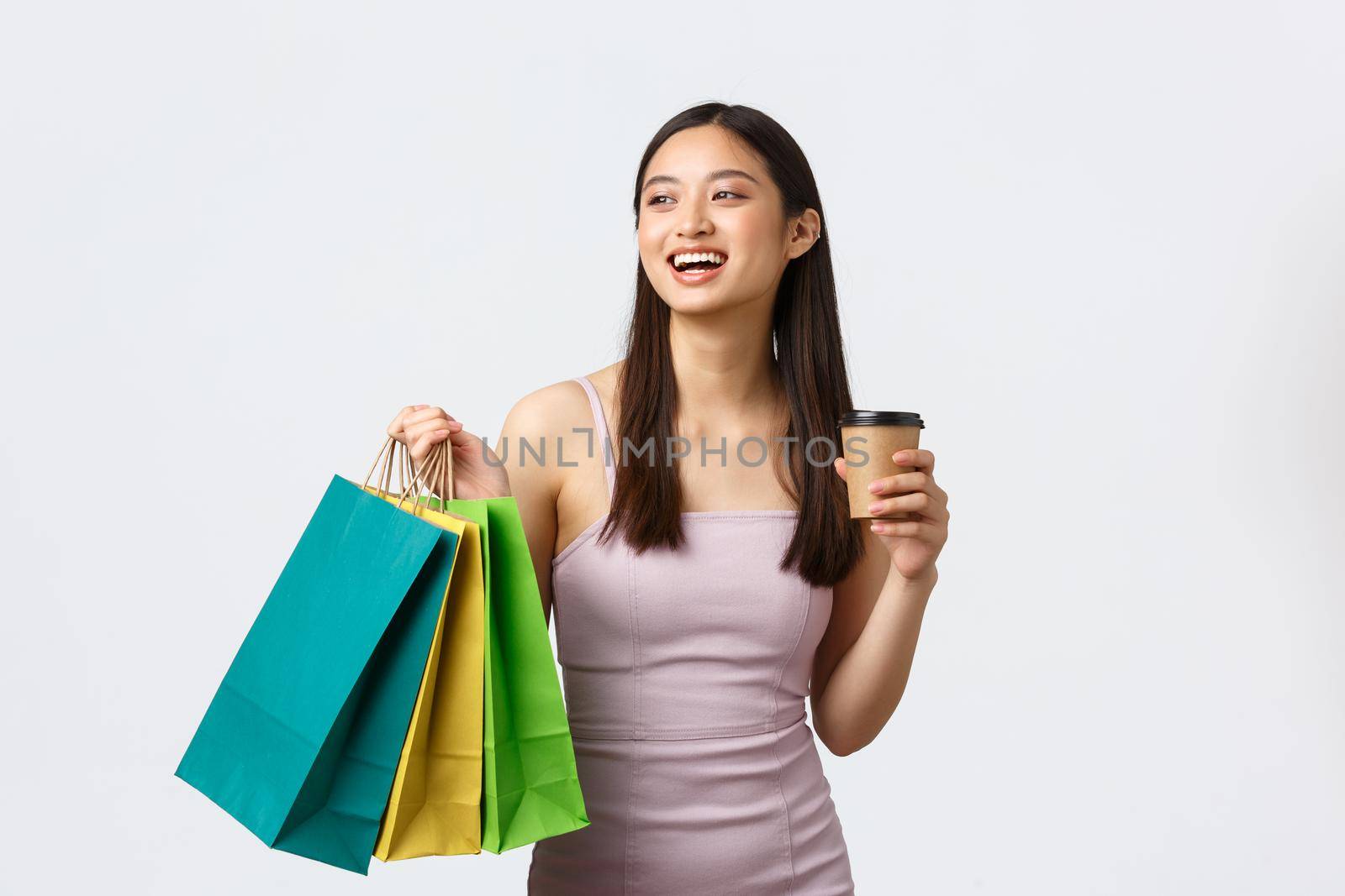 Lifestyle, shopping and tourism concept. Carefree young elegant woman in dress, enjoying weekend, drinking coffee on her way to next shop, carry bags with new clothes, white background by Benzoix