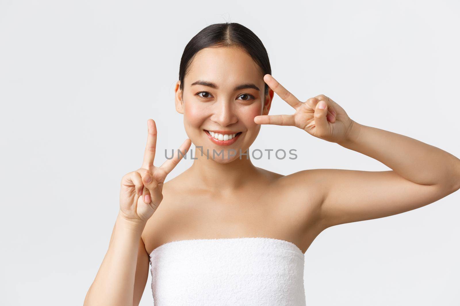 Beauty, cosmetology and spa salon concept. Happy gorgeous asian girl in towel showing kawaii peace gesture and smiling satisfied after beauty clinic, massage therapy, feeling fresh and energized.