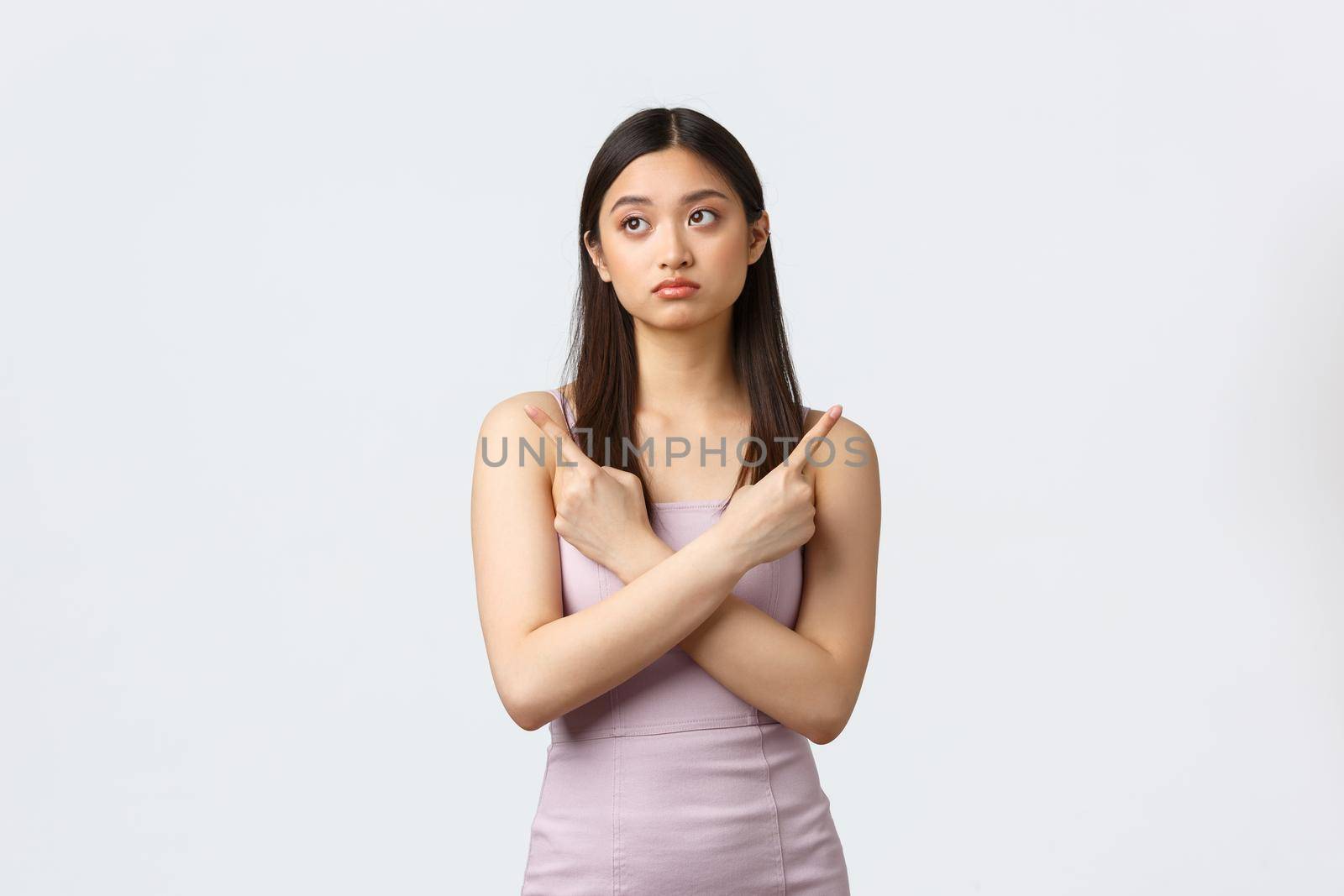 Luxury women, party and holidays concept. Indecisive pretty asian girl in evening dress making tough decision, pointing fingers sideways at both variants, being confused, white background by Benzoix