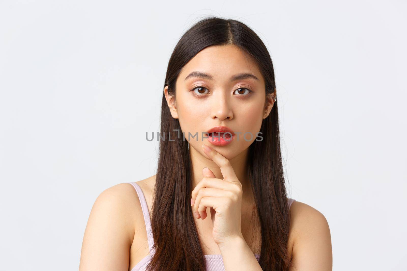 Beauty, fashion and people emotions concept. Close-up portrait of intrigued asian woman listening closely, touch chin and open mouth while looking curious camera, white background by Benzoix