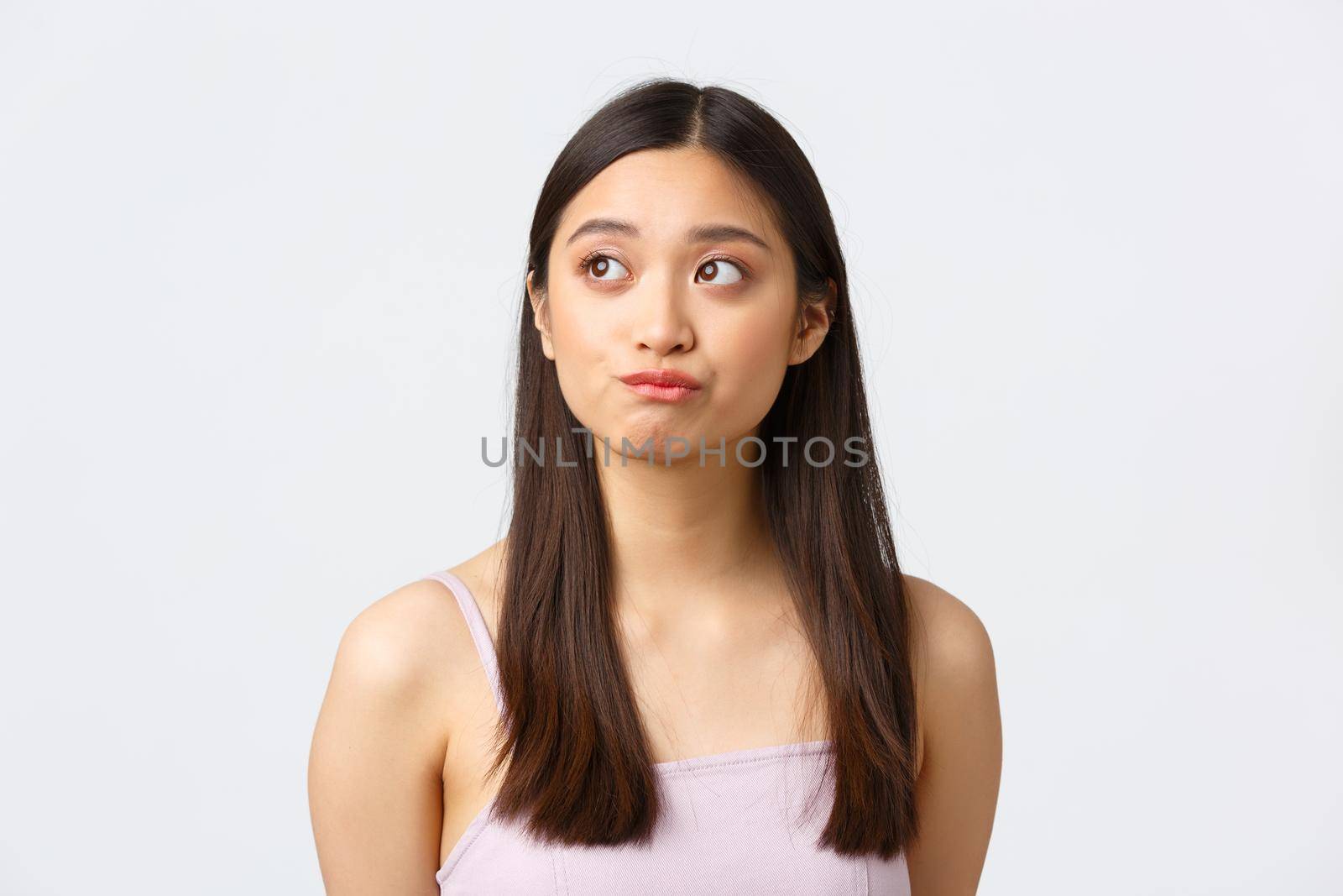 Concept of beauty, fashion and makeup products advertisement. Close-up portrait of beautiful indecisive asian girl having doubts, looking left and smirk unsure, hesitating over white background.