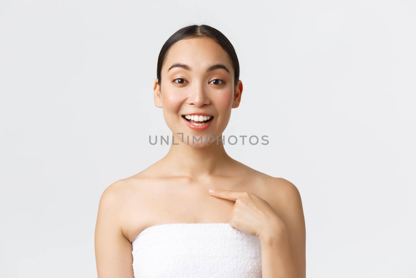Beauty, cosmetology and spa salon concept. Close-up of satisfied beautiful asian female client in white towel smiling and pointing at herself, recommend beauty clinic and skincare procedures.