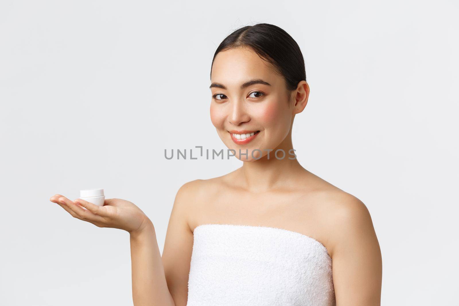 Beauty, personal care, spa salon and skincare concept. Close-up of beautiful asian woman in bath towel introduce facial cream, moisturizing or hydrating treatment for face, skin nourishing.