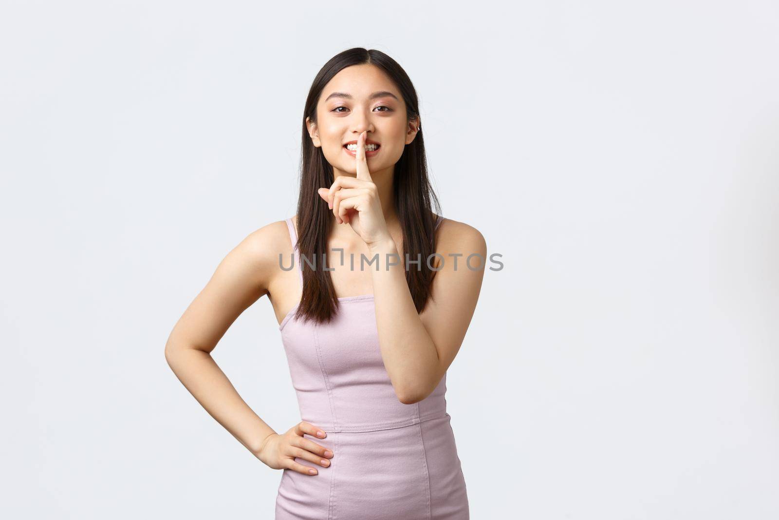 Celebration, beauty and glamour concept. Cute and silly cheerful korean girl in prom dress, attend party or holiday event, shushing with happy smile, prepare surprise, white background by Benzoix