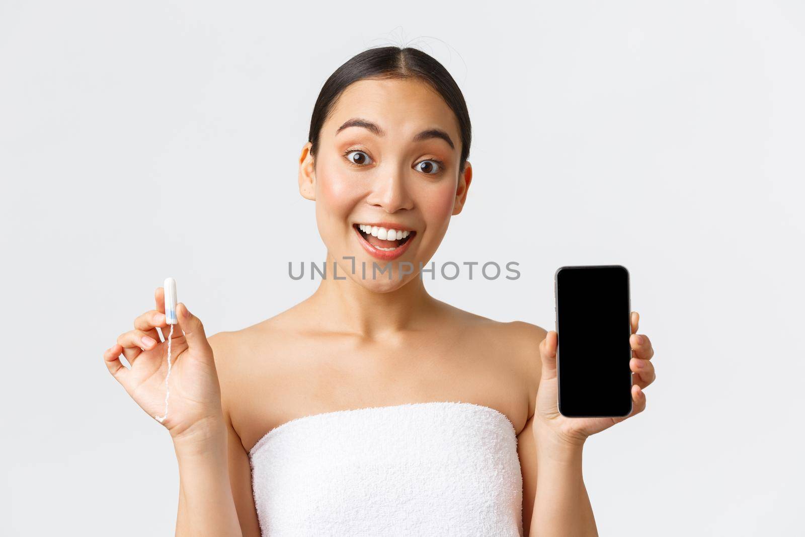 Beauty, personal and intimate care, mobile application concept. Cheerful smiling asian woman showing her menstrual cycle, period tracker on smartphone screen, holding tampon by Benzoix