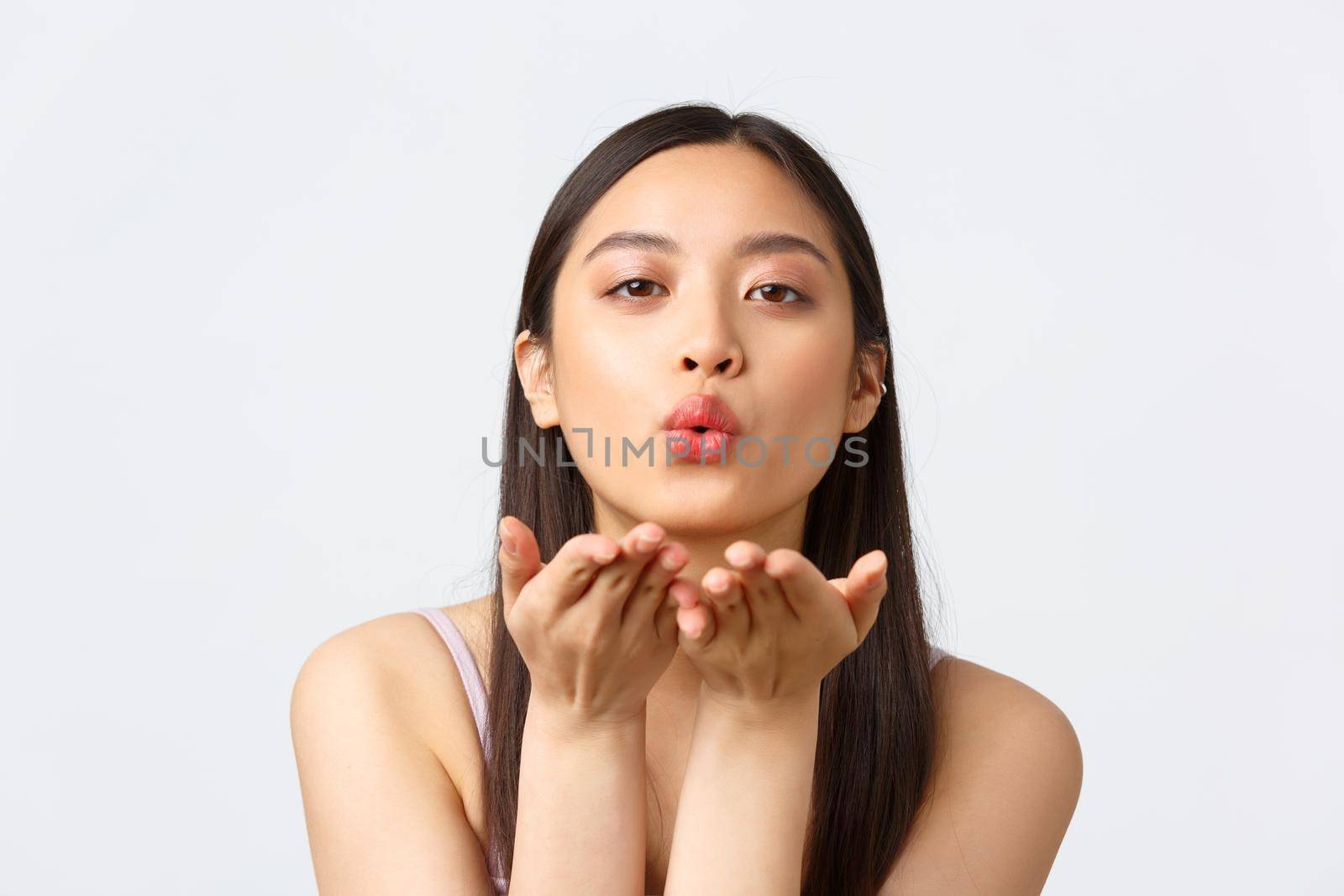 Beauty, fashion and people emotions concept. Close-up portrait of passionate, romantic asian woman sending air kiss at camera, looking lovely, standing white background. Copy space