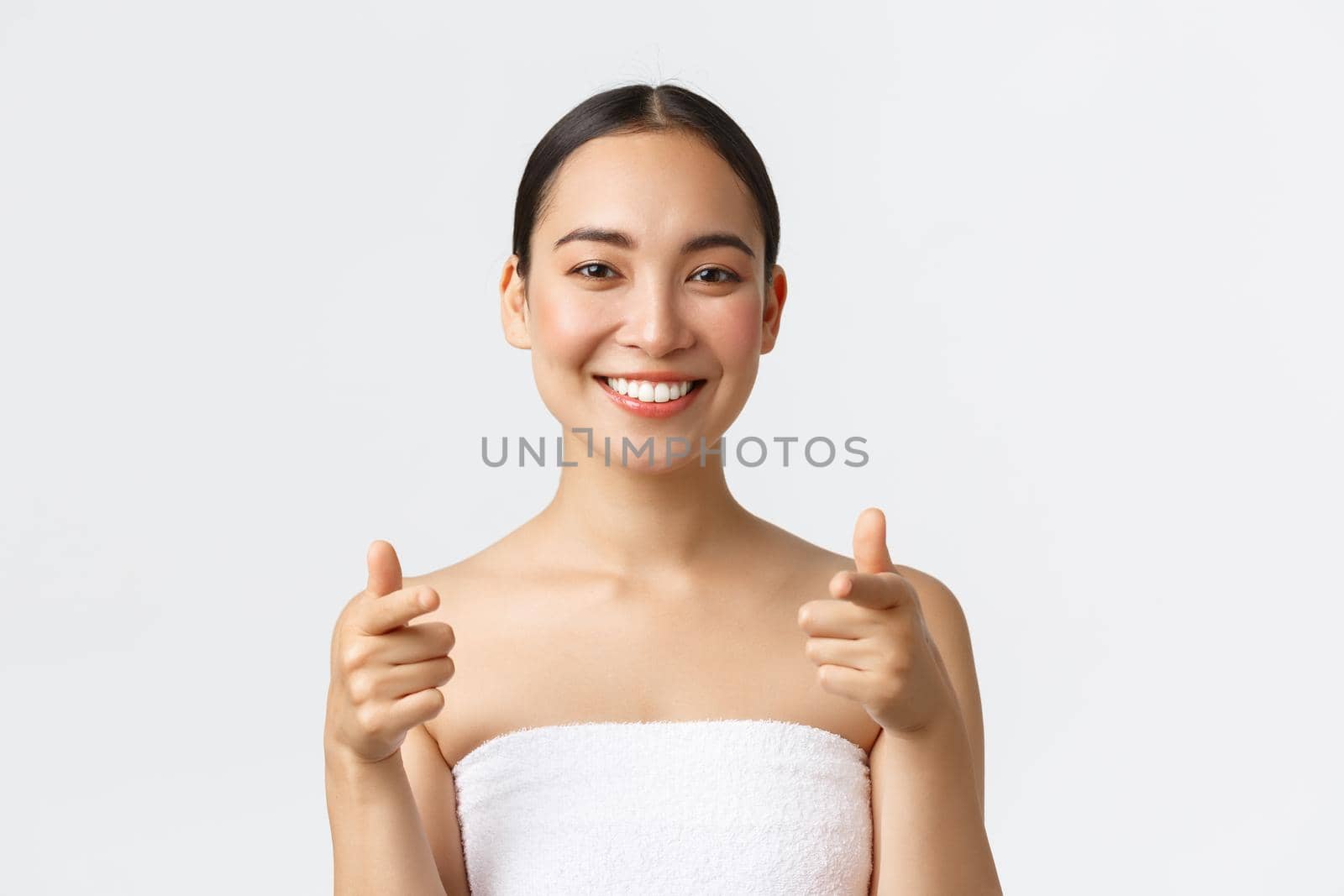 Beauty, cosmetology and spa salon concept. Close-up or attractive asian woman in towel smiling happy and pointing finger at camera, recommend you visit beauty clinic, white background by Benzoix