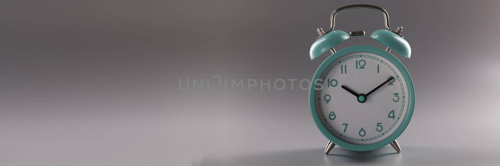 Turquoise alarm clock at ten o'clock on gray background. Time control concept