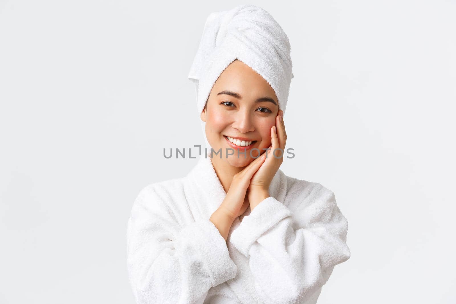 Personal care, women beauty, bath and shower concept. Close-up of beautiful happy asian woman in towel and bathrobe touching face gently, smiling white teeth, promo of skin care and hygiene products.