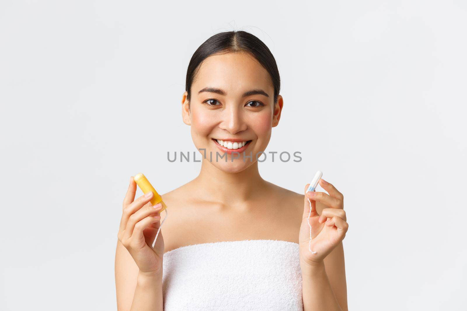 Beauty, personal and intimate care menstrual hygiene concept. Close-up of attractive asian girl in towel showing tampon with and without applicator, smiling at camera, white background by Benzoix