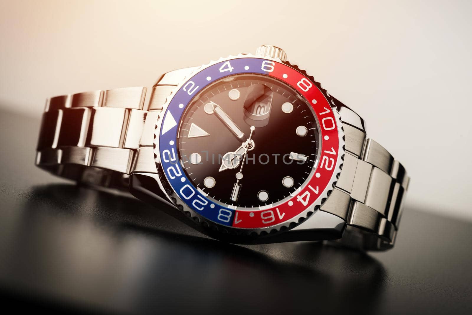 closeup luxury wristwatch for men with black dial blue-red bezel and stainless steel bracelet.