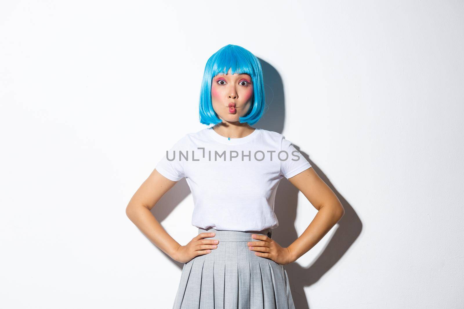 Portrait of beautiful korean girl pouting coquettish, looking at camera silly, standing in blue wig and party costume for halloween.