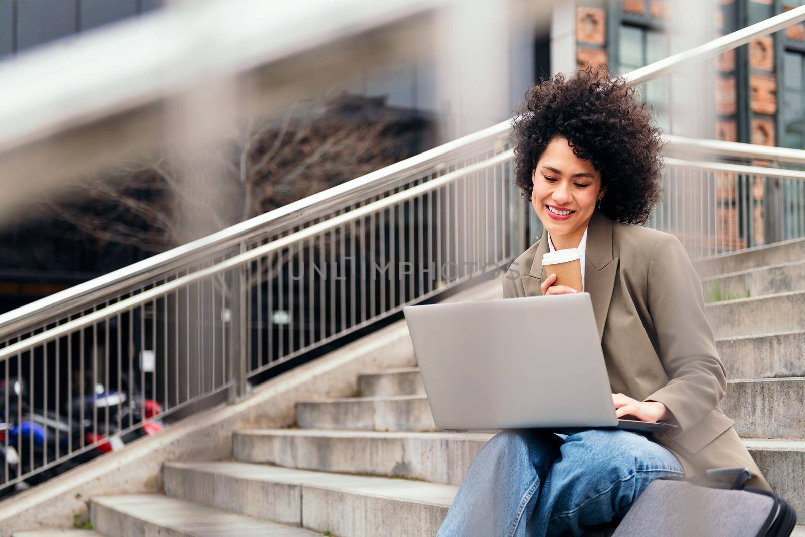 happy young woman sitting in the city with a coffee and working on her laptop computer, concept of business and urban lifestyle, copy space for text