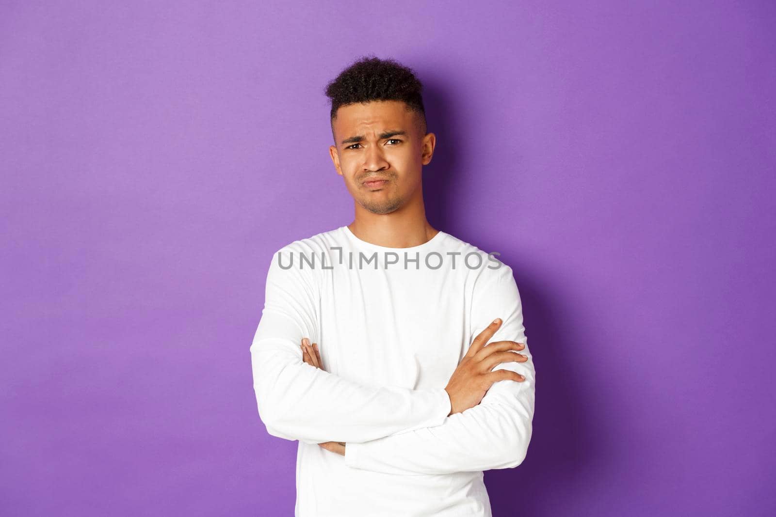 Portrait of skeptical african-american man looking with disbelief, cross arms on chest and frowning doubtful, standing over purple background by Benzoix