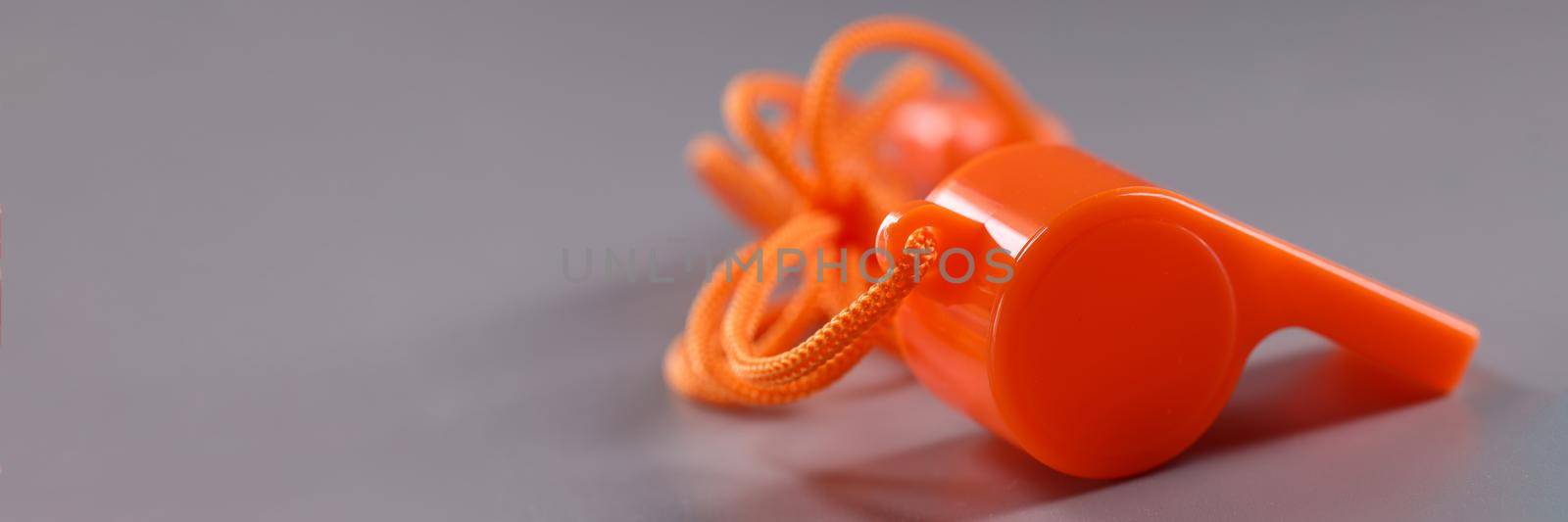 Orange plastic whistle with rope on gray background by kuprevich