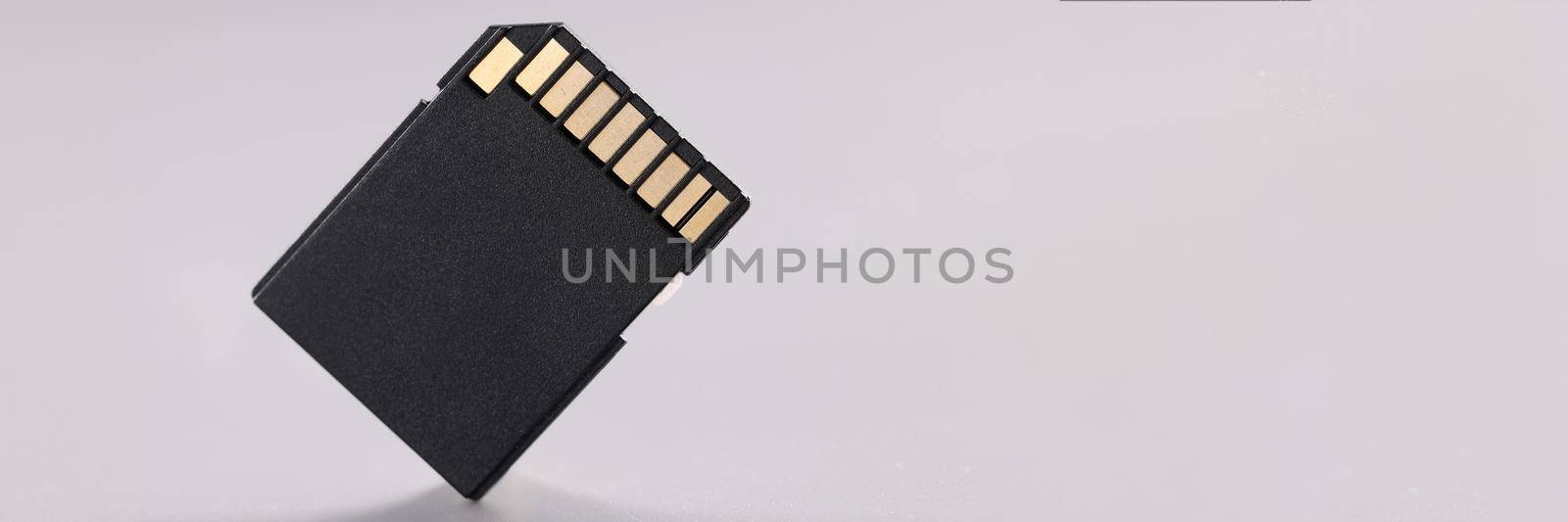 High quality black sd memory card with small gold disc on gray background. Small portable electronic memory card concept