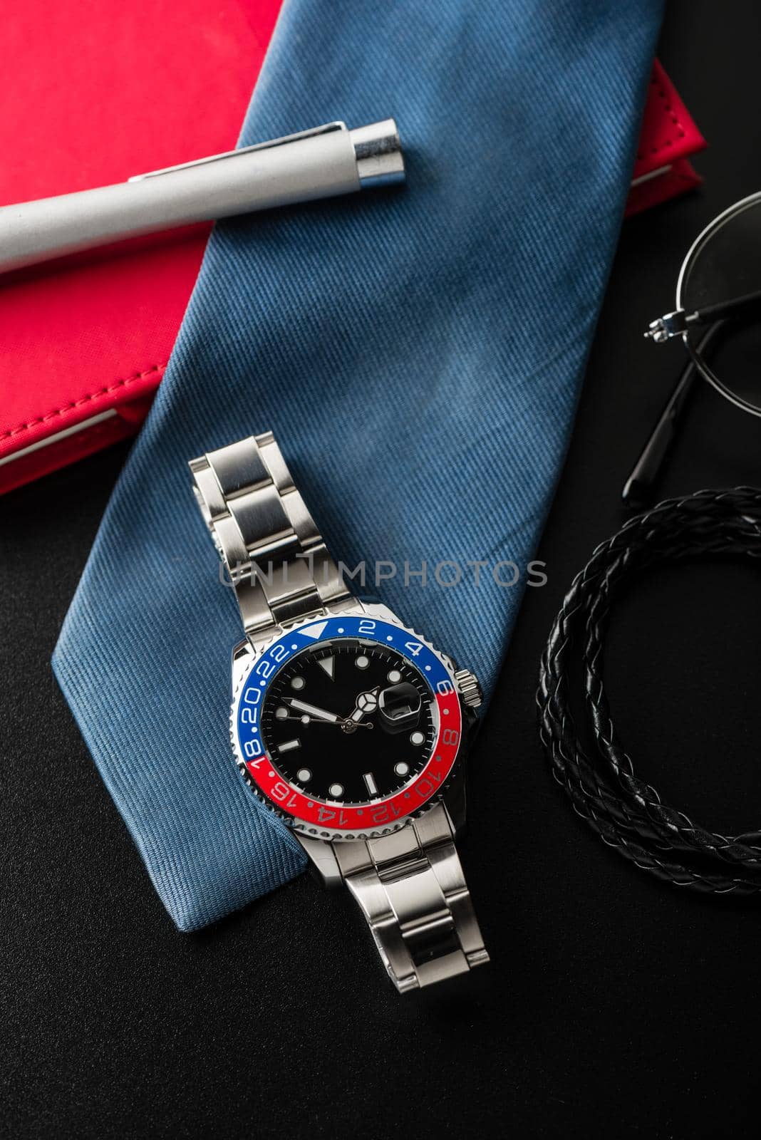 closeup luxury wristwatch for men with black dial blue-red bezel and stainless steel bracelet.