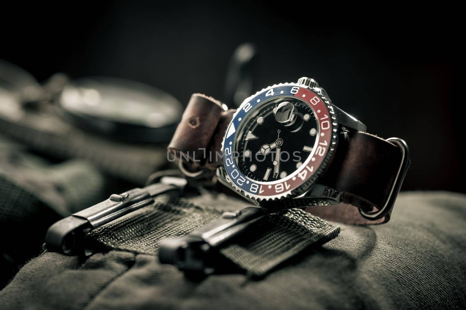 closeup luxury wristwatch for men with black dial blue-red bezel and leather strap. wristwatch with vintage men's objects.