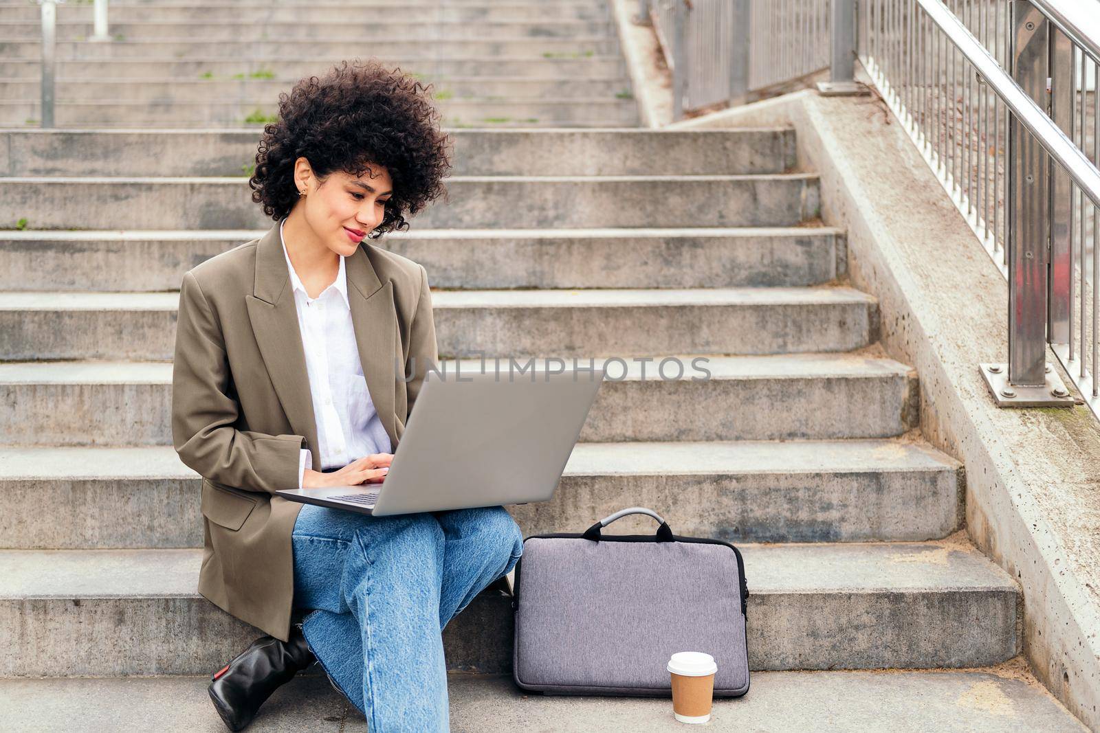 young latin woman working with her laptop computer sitting on a city staircase, concept of business and urban lifestyle